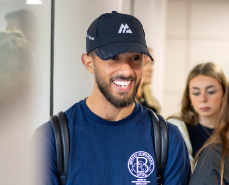An apprentice in a blue t-shirt and cap, smiling as they walk through the building